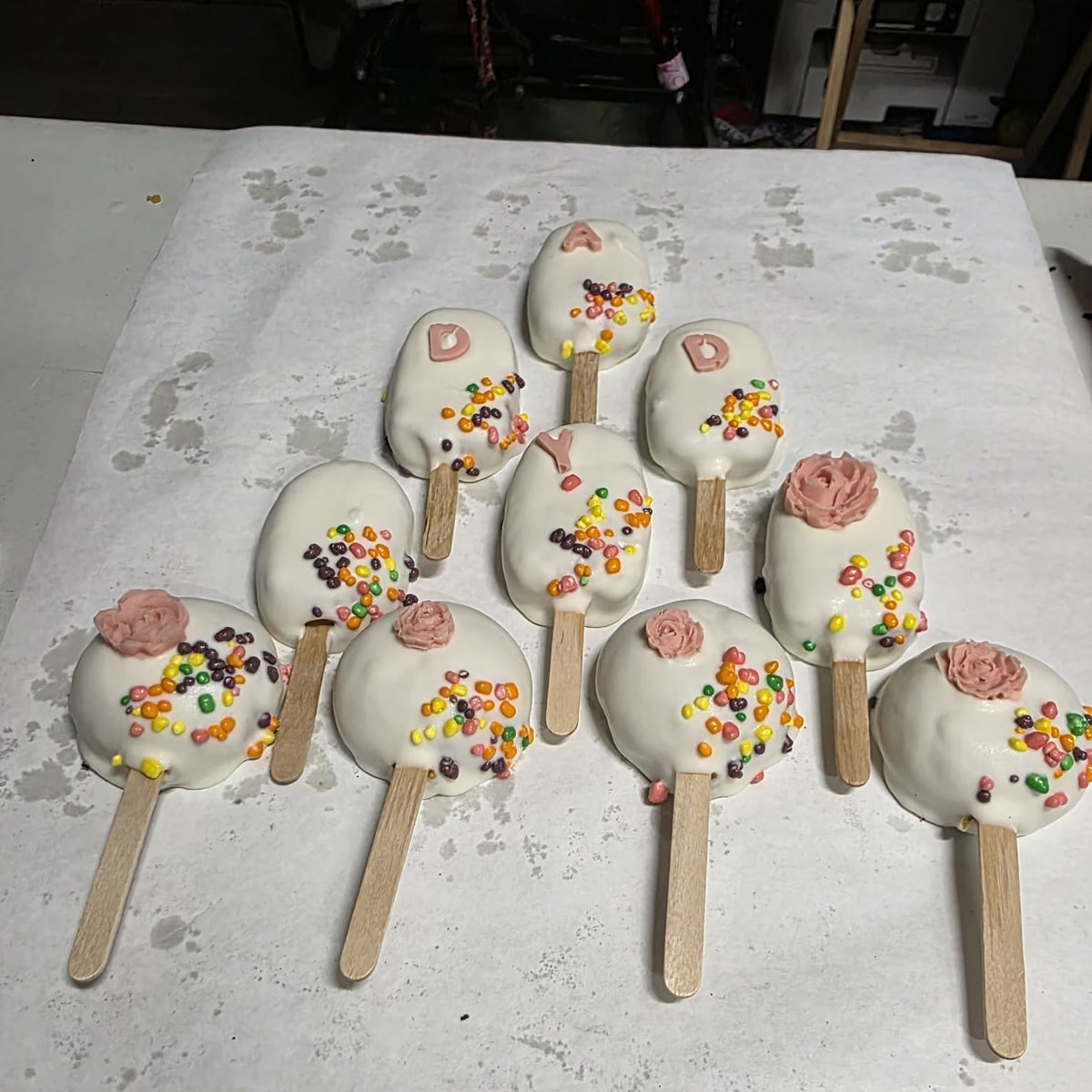 Hand-decorated white chocolate cakesicles with sprinkles and frosting roses, made as a custom gift set