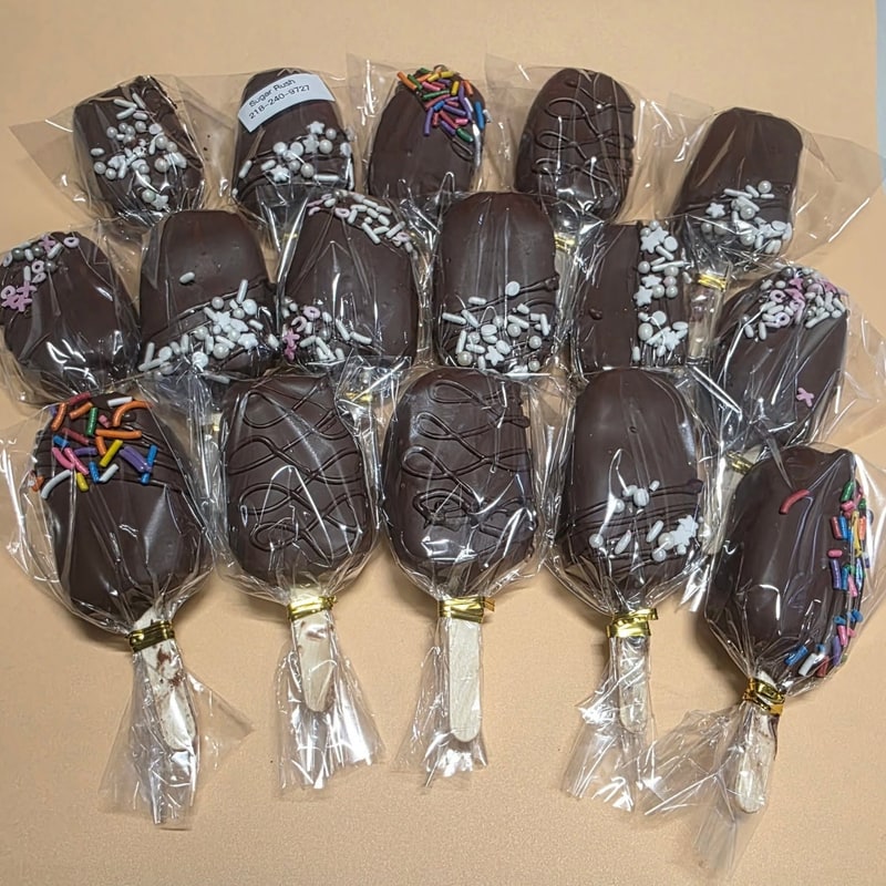 Chocolate-dipped cakesicles with sprinkles arranged on a table