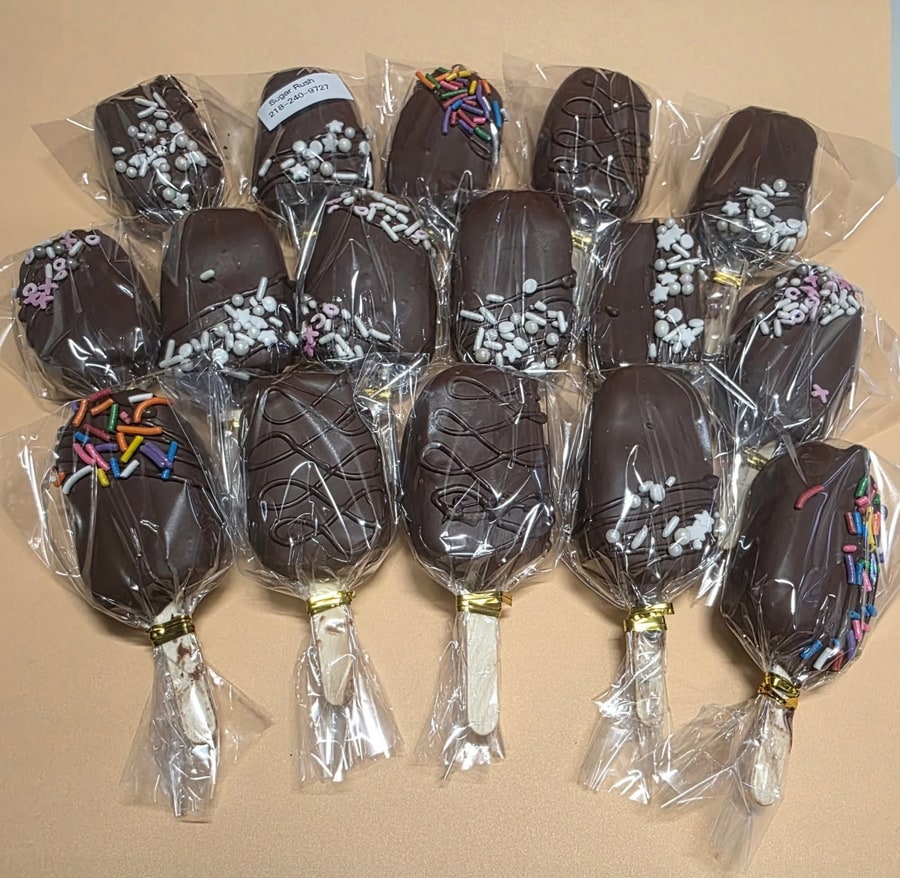 Rows of chocolate-dipped cakesicles with white and rainbow sprinkles