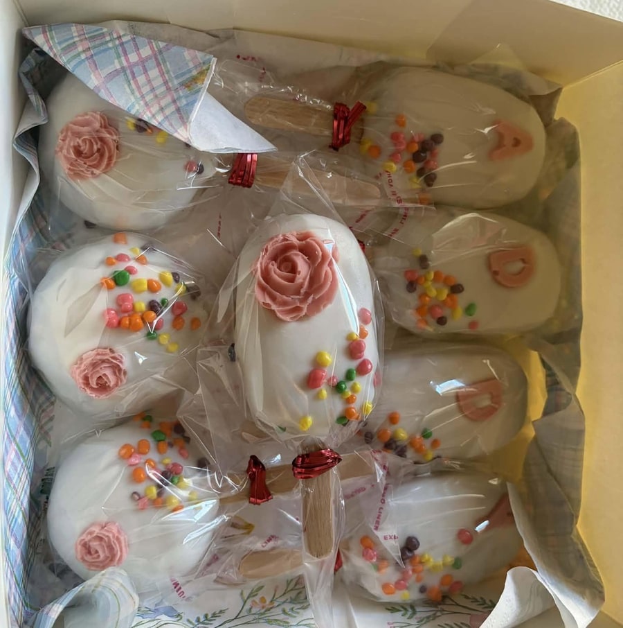 Gift box of white chocolate cakesicles decorated with pink frosting roses and candy