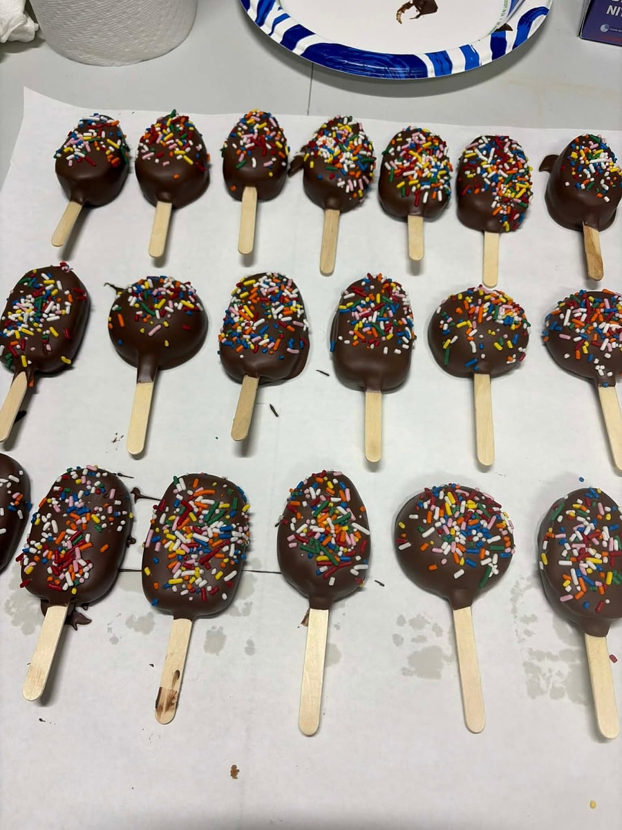 Chocolate cakesicles with rainbow sprinkles lined up on parchment
