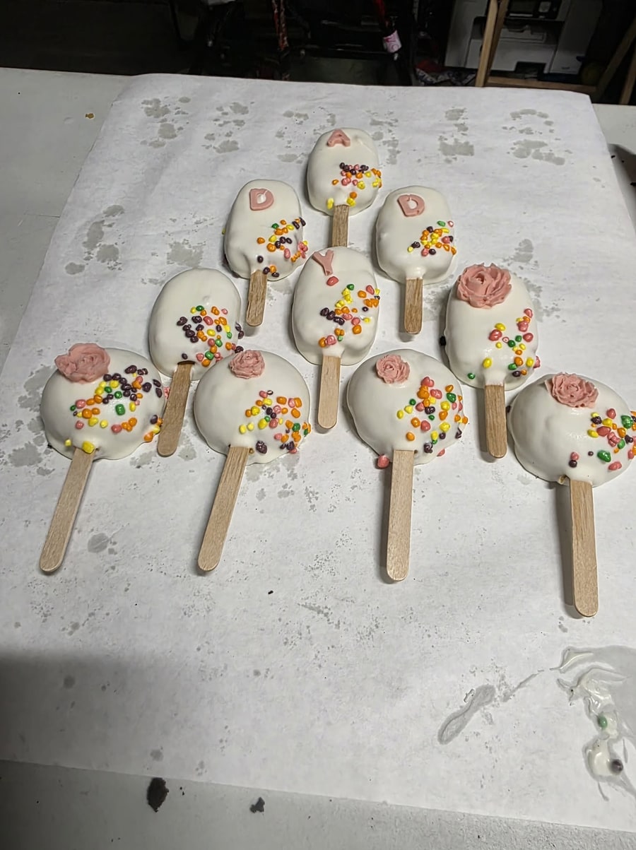 White cakesicles decorated with sprinkles, pink roses, and lettering for a custom order