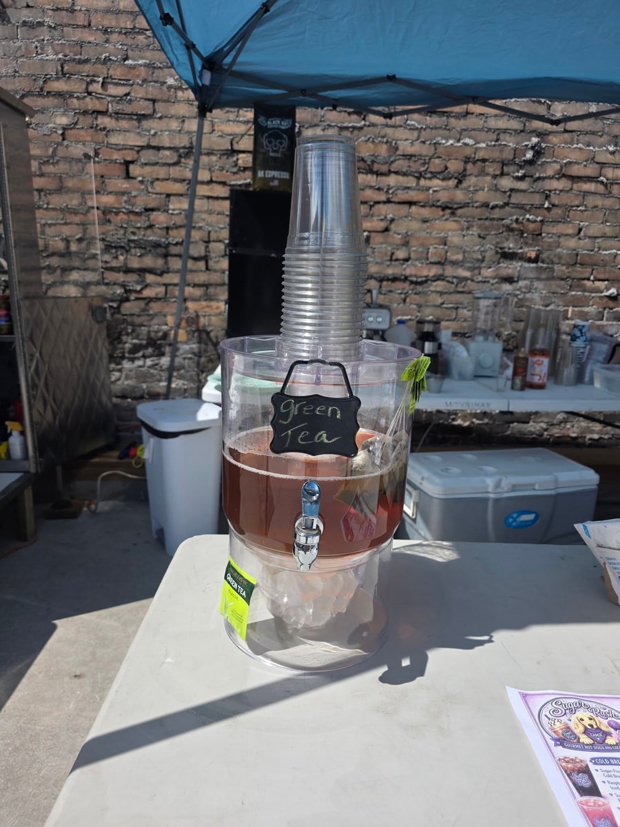 Iced green tea dispenser and cups set up under a canopy at an outdoor event