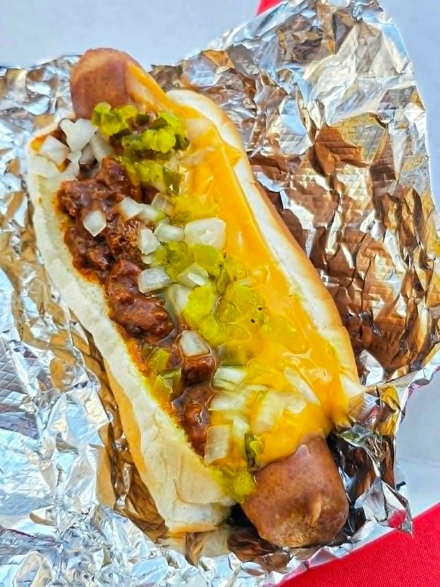 Loaded hot dog topped with chili, melted cheese, diced onion, and relish