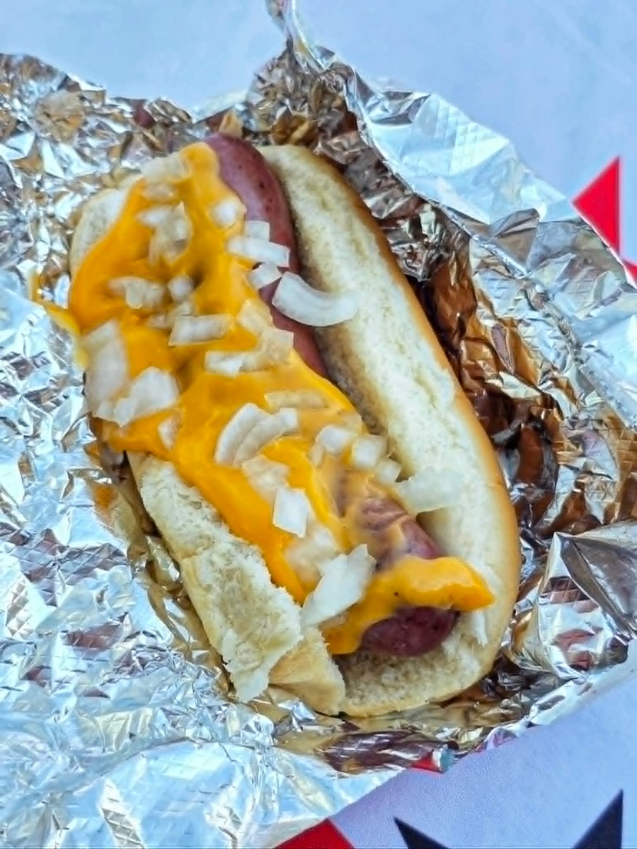 Cheddar brat topped with melted cheese and diced white onion