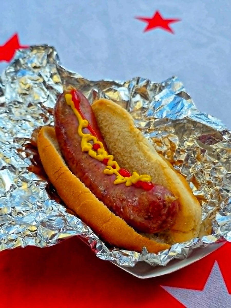 Classic brat in a bun with a mustard drizzle, wrapped in foil
