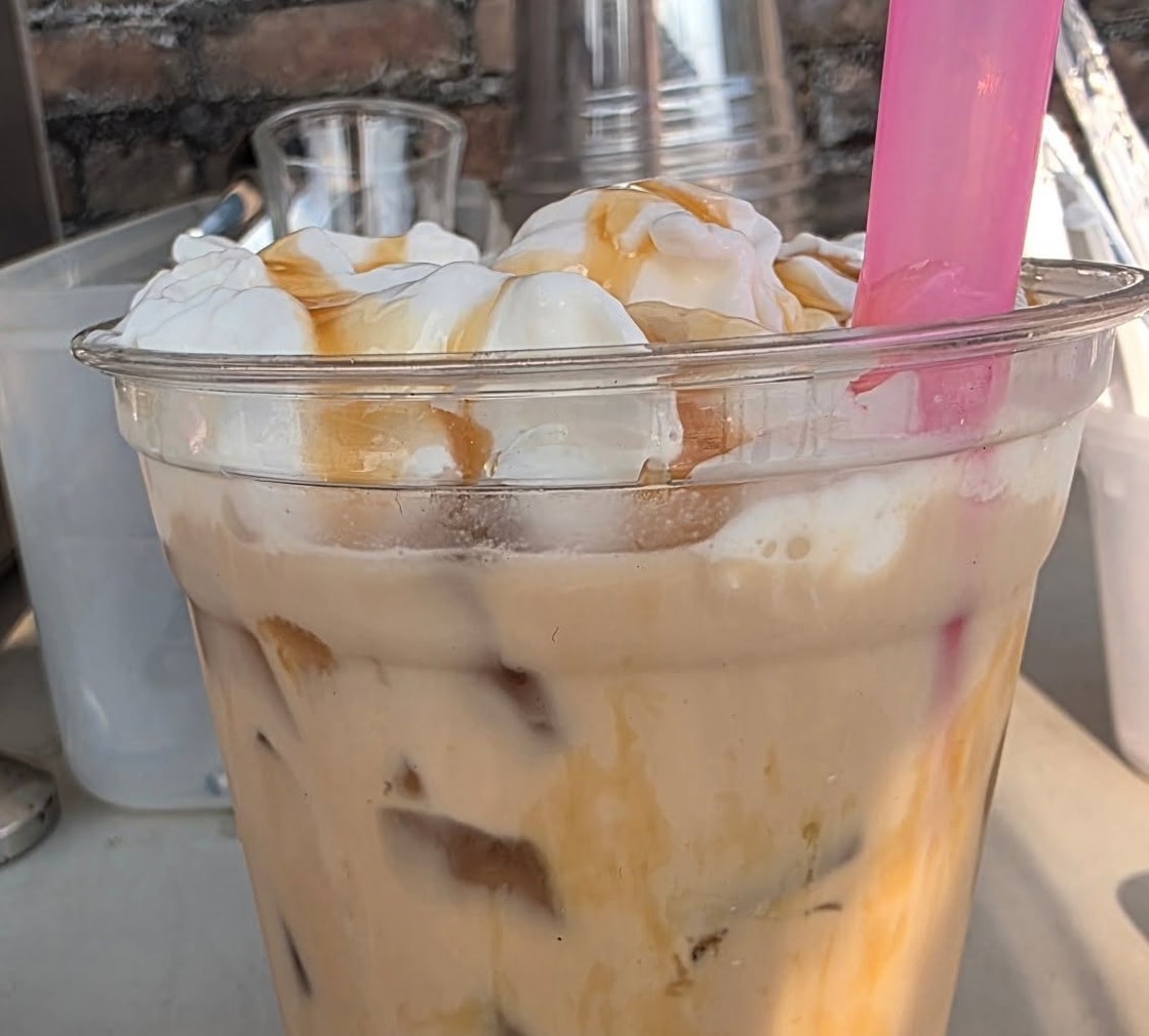Iced caramel coffee with whipped cream and caramel drizzle in a clear cup with a pink straw